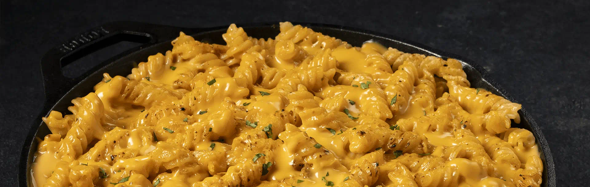 Rotini pasta in a cast‑iron pan, covered in dairy free cheese sauce with a few herbs sprinkled on top.